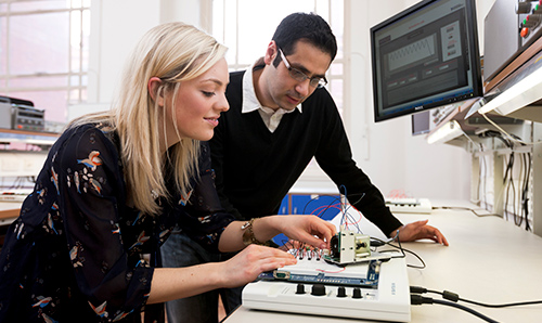 Two researchers demonstrating how to use intricate electrical equipment