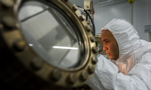 Man in full protective suit peering into a piece of equipment