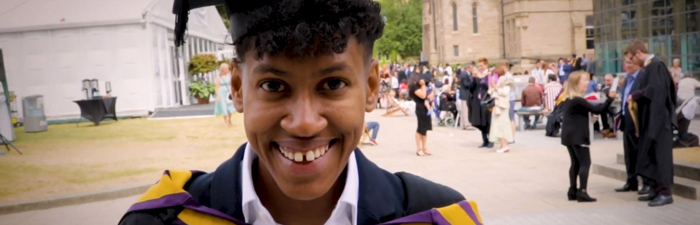A student smiles at the camera, wearing a black graduation cap and gown.