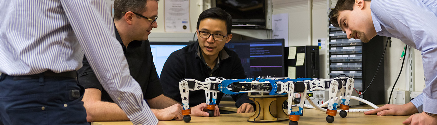 A group of researchers in discussion around a robot spider