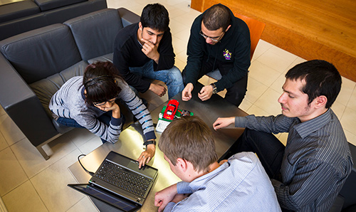 A group of people sat around a laptop and an electric car prototype