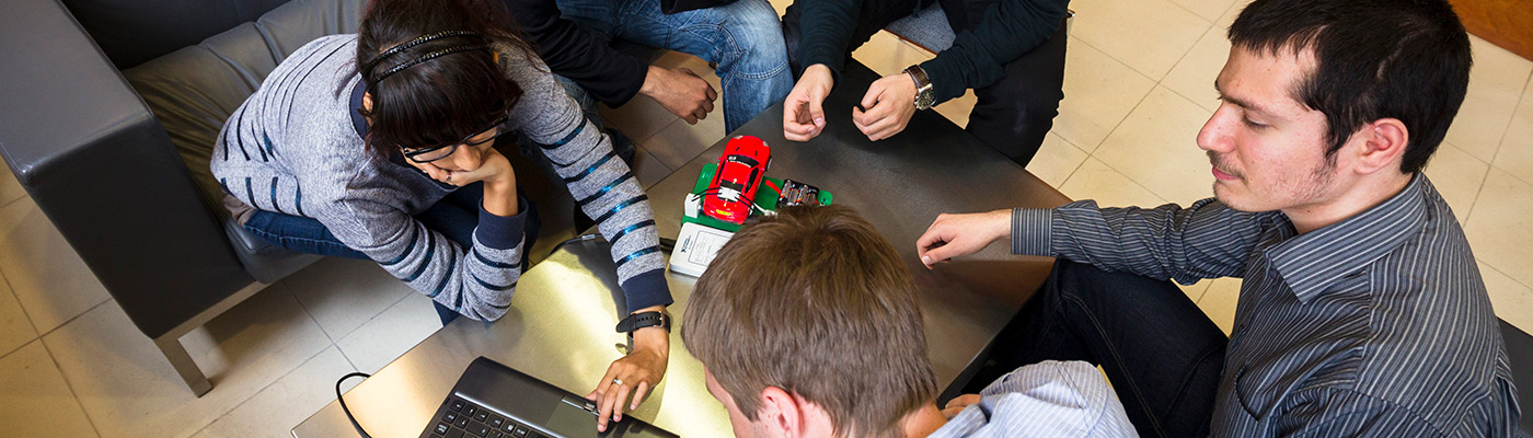 A group of people sat around a laptop and an electric car prototype
