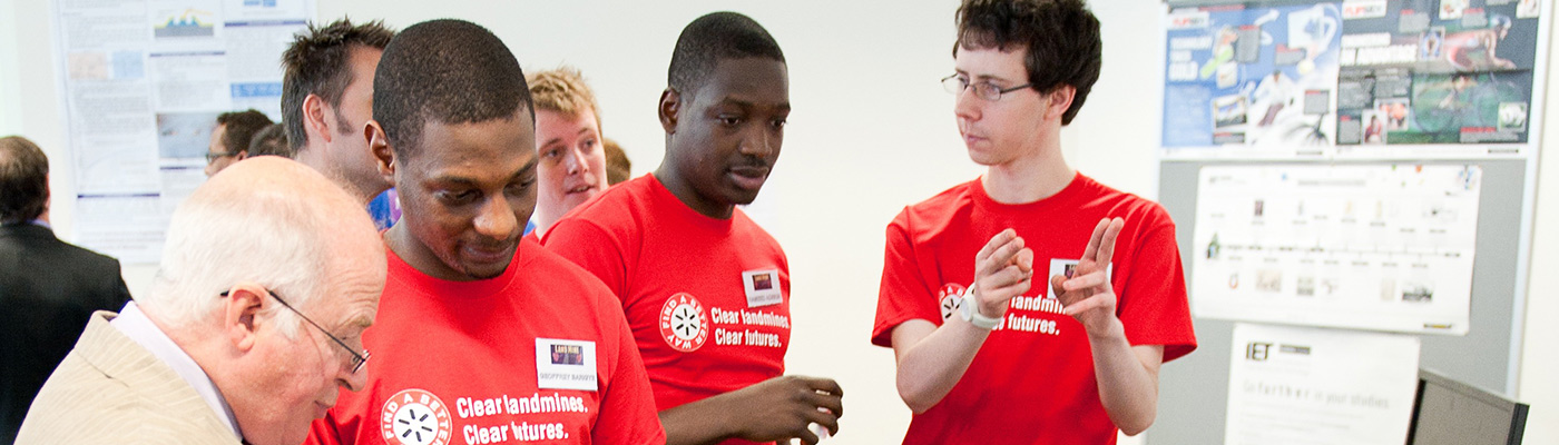 Three students and a professor in discussion at electronic engineering project presentation