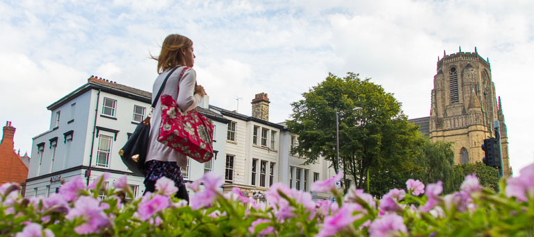 A woman walking next to flowers and the University 