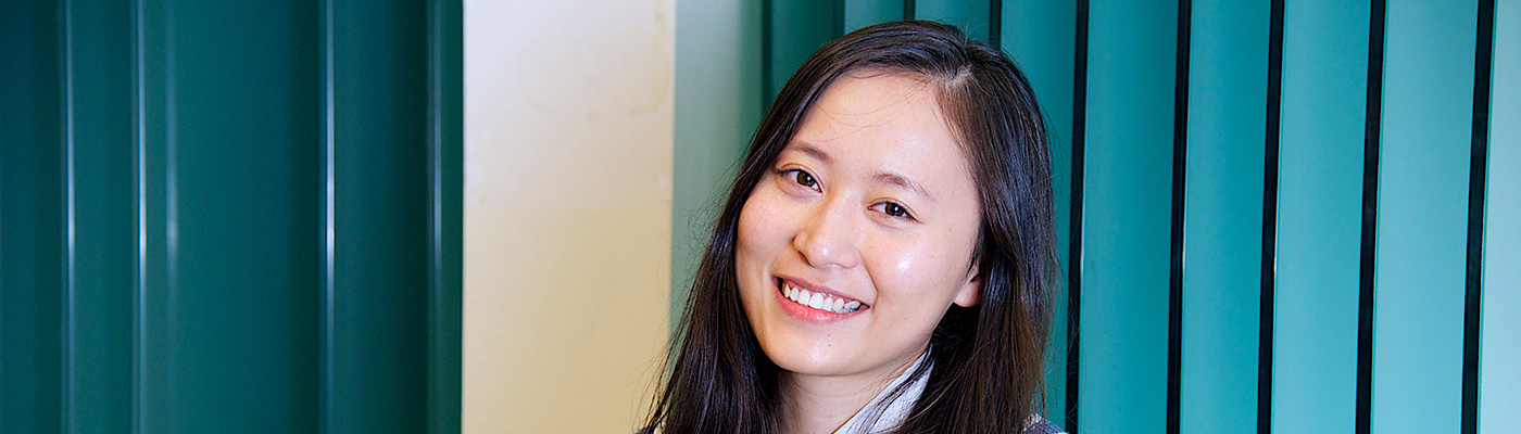 Female student smiling at the camera in front of turquoise background