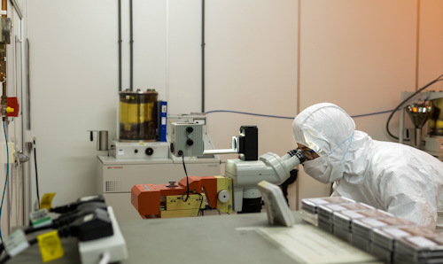 Person in full-body white lab suit looking into a microscope