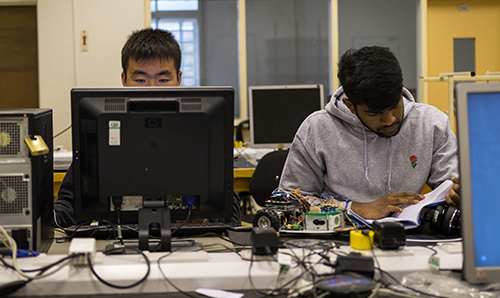 Two students; one using a computer, the other reading a book